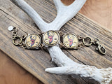 Handcrafted brass link bracelet with three vintage gold buck head bottle caps displayed across an antler on a wood background 