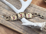 Handcrafted square brass link bracelet with three vintage red and gold buck head bottle caps displayed on an antler and wood board background