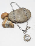 A buffalo nickel medallion on a gold paper clip chain necklace, displayed on a rock.