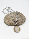 A buffalo nickel medallion on a gold paper clip chain necklace, displayed on a rock.