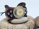 A leather cuff bracelet with a concho featuring a 12g shotgun casing, positioned on a rock.
