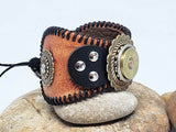 Side view of leather cuff bracelet with a concho featuring a 12g shotgun casing, positioned on a rock.