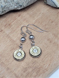 Pair of brass 9mm bullet casing dangle earrings with silver round beads displayed on a wood background.