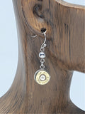 Close up of brass bullet casing dangle earring on wood ear mannequin.