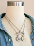 Stainless steel thin paperclip chain necklaces each with 20 gauge shotshell pendants, one in brass and one with a nickel casing, shown on a mannequin.