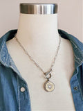 Stainless steel thin paperclip chain necklace with brass 20 gauge shotshell pendant, displayed on a mannequin wearing a blue denim shirt.