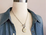 Stainless steel thin paperclip chain necklace with brass 20 gauge shotshell pendant, displayed on a mannequin wearing a blue denim shirt.