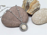 Close up of round stainless steel beaded bezel nickel bullet pendant displayed on a rock with stainless beaded chain.