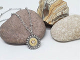 Close up of round stainless steel beaded bezel nickel bullet pendant displayed on a rock with stainless beaded chain.