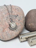 A stainless steel bullet necklace with a pendant featuring a trimmed caliber design, displayed on a rock.