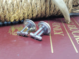 Photo of pair of cuff links displayed on a burguny book with rope and antler in background showing the back side of the cuff links.