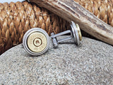 Pair of brass Winchester 45 Colt bullet casing cuff links displayed on a stone with a rope and antler in background. One cuff links is facing sideways.