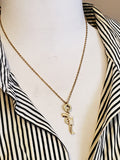 Gold pistol bullet necklace worn on mannequin with striped shirt, featuring petite pavé pistol charm and .22 Hornet casing ring connector