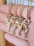 Group of gold pistol charm bullet necklaces hanging together, displayed against an open hand showing SureShot Jewelry .22 Hornet casing details