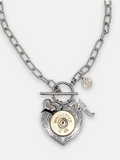 Photo of a 12 gauge shotshell mounted on a heart shaped pendant flanked with a puffy heart charm and pistol charm flat layed on a white background.