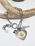 Paper clip chain style bracelet with heart and pistol charms and a focal heart pendant with a 20 gauge brass shotshell.  Bracelet is displayed across a deer antler on an otherwise white background.
