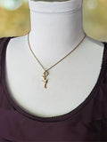 Gold pave encrested petite pistol charm hung from a 22 hornet bullet casing with primer removed to be a ring connector, hung on a delicate gold stainless cable chain, shown on a white mannequin wearing a plum colored tank top.