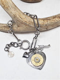 Paper clip chain style bracelet with heart and pistol charms and a focal heart pendant with a 20 gauge brass shotshell.  Bracelet is displayed across a deer antler on an otherwise white background.