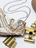 Tiny stainless heart pendant displayed on a striped rock with .22 caliber brass bullet casings surrounding it.  Heart has "Rem" brass headstamp mounted to it.