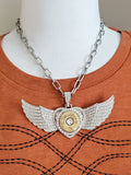 Front view of large pavé winged heart necklace featuring a brass 12 gauge shotshell and faceted crystal center worn on mannequin with an orange t-shirt.