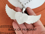 Back view silver toned large winged heart pendant with large matching bail on a paperclip chain being held in a hand to show scale.