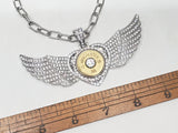 Close up of pave encrusted winged heart statement pendant necklace shown with a brown wood ruler to show the span of the wings being about 4 inches in length.  Necklace and ruler are on a white background.