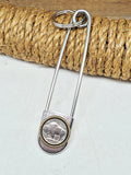 5 inch jumbo stainless steel safety pin leaning on a roll of tan rope on a white background.  Safety pin is embellished with a genuine buffalo nickel coin mounted in a brass rope edge bezel.