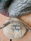 Lightweight goose band earrings with turquoise beads displayed on natural stone and wood and photographed further away and directly above the earrings.  There is a duck decoy partially in the photo and everything is sitting on a wood base.  Photo shows authentic numbered aluminum bird bands and stainless steel ear wires.