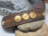 Vintage Ducks Unlimited leather cuff displayed open across smooth stones with a painted duck decoy behind it. Three bronze Sponsor medallions are mounted across the western tooled leather and gold snap hardware is visible at both ends.