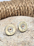 Pair of Winchster brand 28 gauge brass shotshell stud earrings displayed on a neutral stone with rope coil in background.