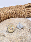 Pair of Winchester brand brass 28 gauge shotshell stud earrings displayed on a neutral color stone with a coil of rope in the background.  One of the earrings is turned upside down to show the stainless steel back and the earring keeper.