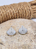 Pair of stud earrings that are turned upside down to show the stainless steel bezels and earring keepers.  They are mounted with brass 28 gauge brass shotshells and displayed on a neutral stone with rope coil in background.