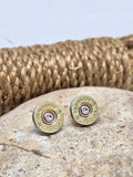 Pair of vintage Remington-Peters brand 28 gauge brass shotshell stud earrings displayed on a neutral stone with rope coil in background.