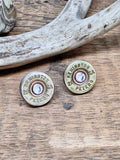 Pair of vintage Remington-Peters brand 28 gauge brass shotshell stud earrings with diamond colored crystals in the centers of each.  The earrings are displayed on a neutral stone with rope coil in background.